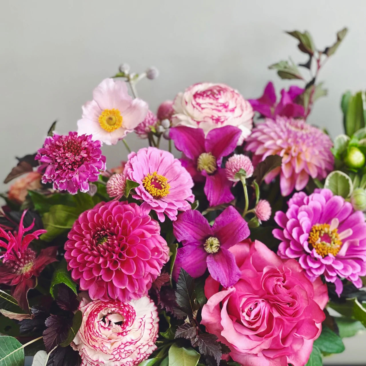 Bouquet of colorful flowers including pink, purple, and white blooms with green leaves on a light gray background from medley flower shop