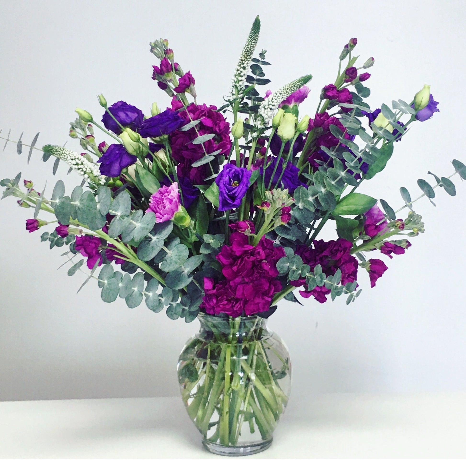 Bouquet of purple and pink flowers in a clear vase on a white background from a flower shop in Surfside for flower delivery