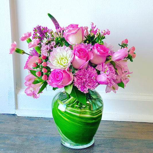 Bouquet of pink and purple flowers in a green vase on a wooden surface for delivery in Miami Dade county