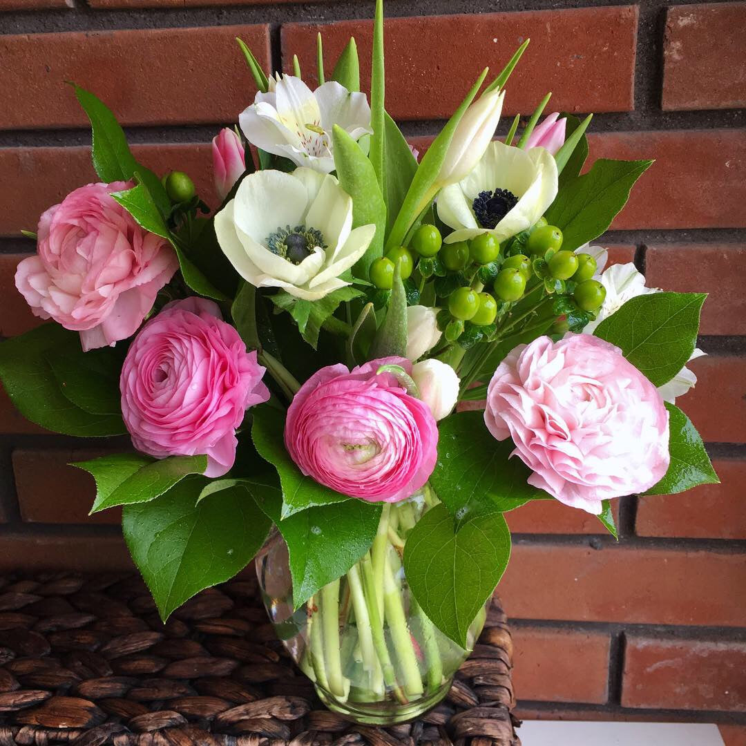Bouquet of pink and white flowers in a glass vase against a brick wall.
