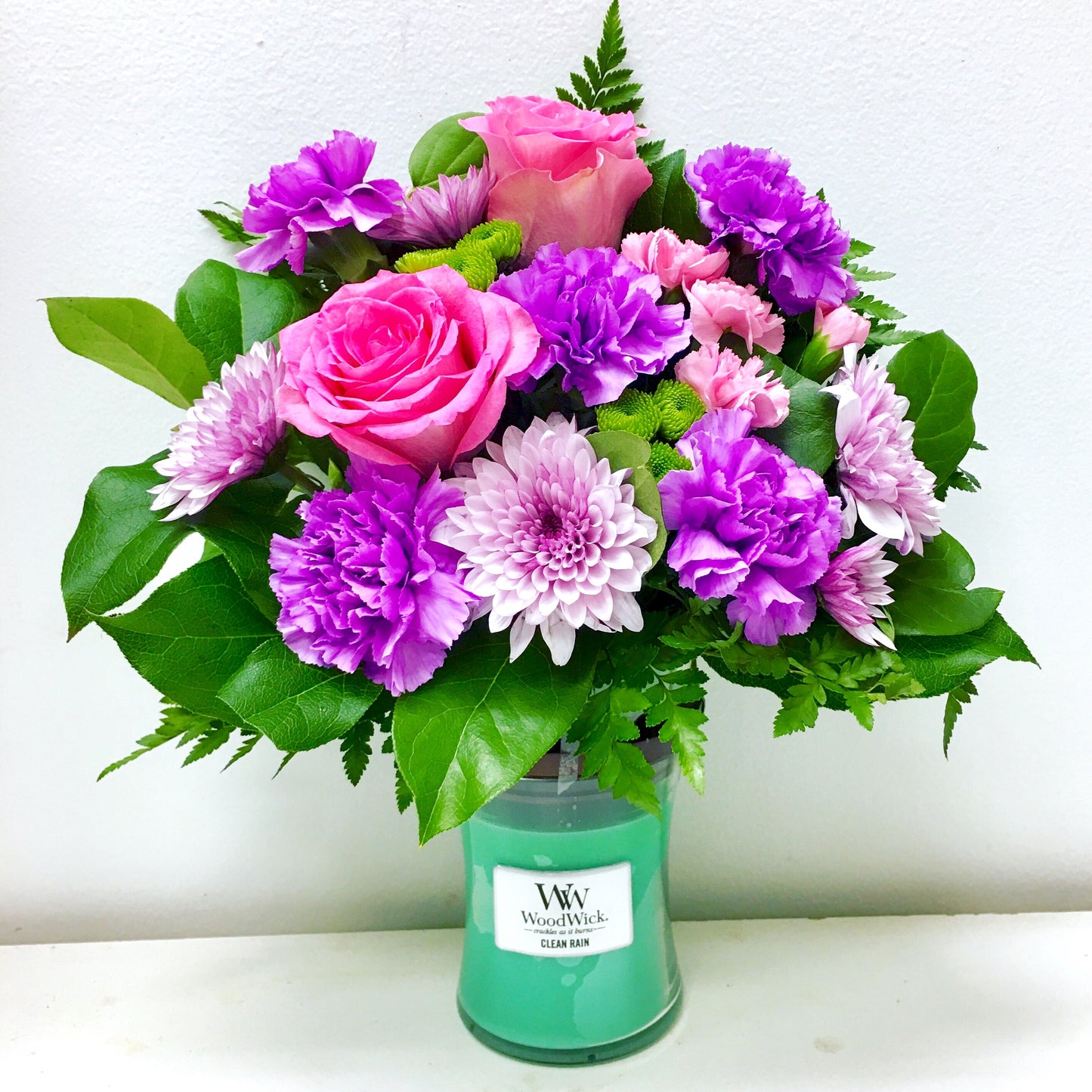 Bouquet of pink and purple flowers in a green candle holder on a white background in Miami flower shop