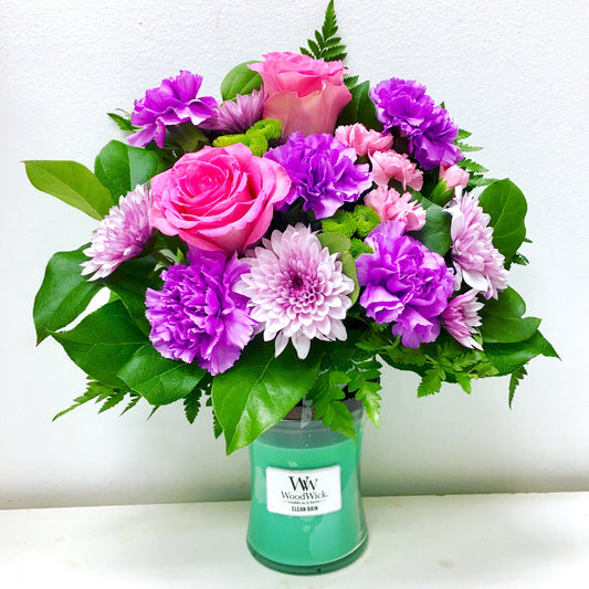 Bouquet of pink and purple flowers in a green candle holder on a white background in Miami flower shop