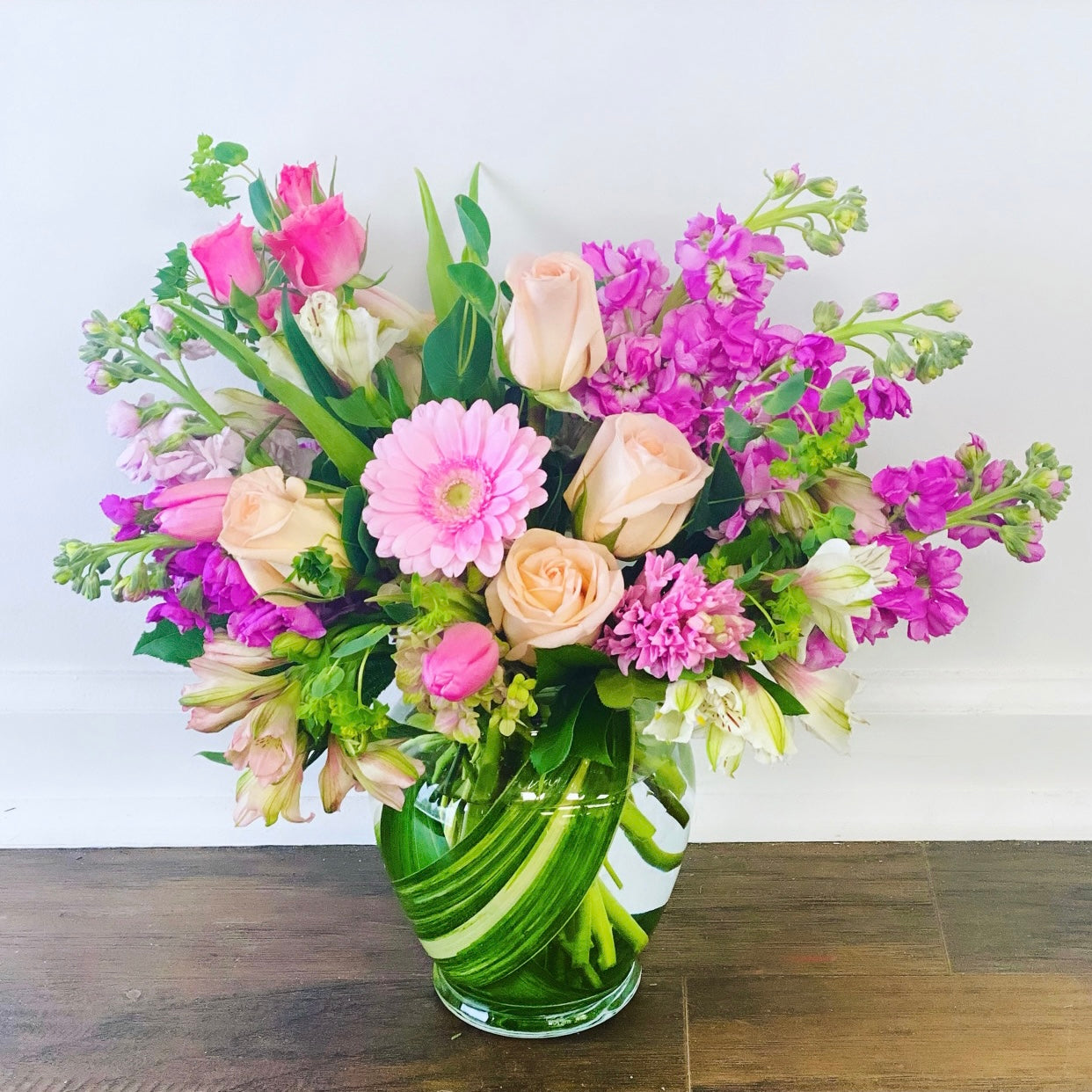 Bouquet of flowers in a green vase on a wooden surface with a white background