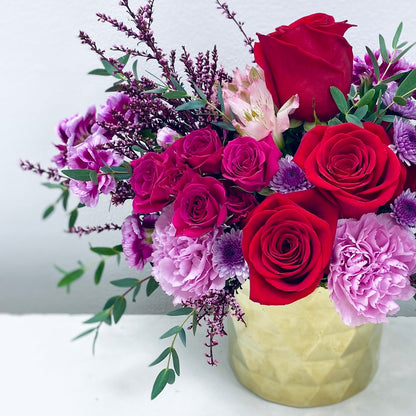 Bouquet of red and pink roses with purple flowers in a gold vase on a white background in south beach Miami Beach 