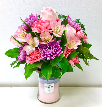 Bouquet of pink and purple flowers in a Trilogy candle container on a white background from Miami florist