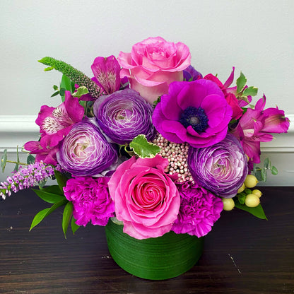 Colorful flower arrangement with pink and purple flowers in a green vase on a wooden surface for flower delivery
