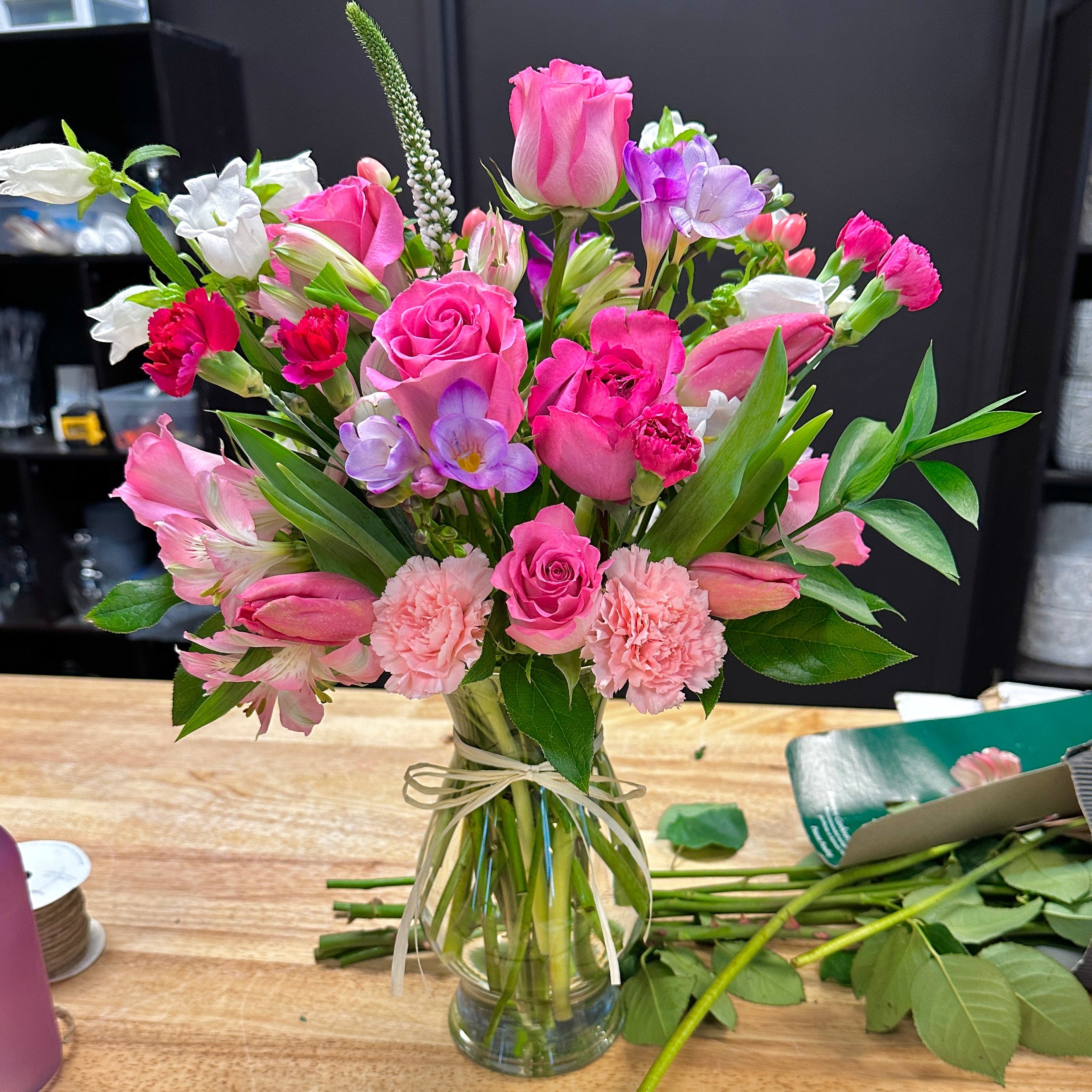 A spring bouquet of flowers in a clear vase for flower delivery on a wooden table  with roses and tulips