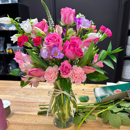 A spring bouquet of flowers in a clear vase for flower delivery on a wooden table  with roses and tulips