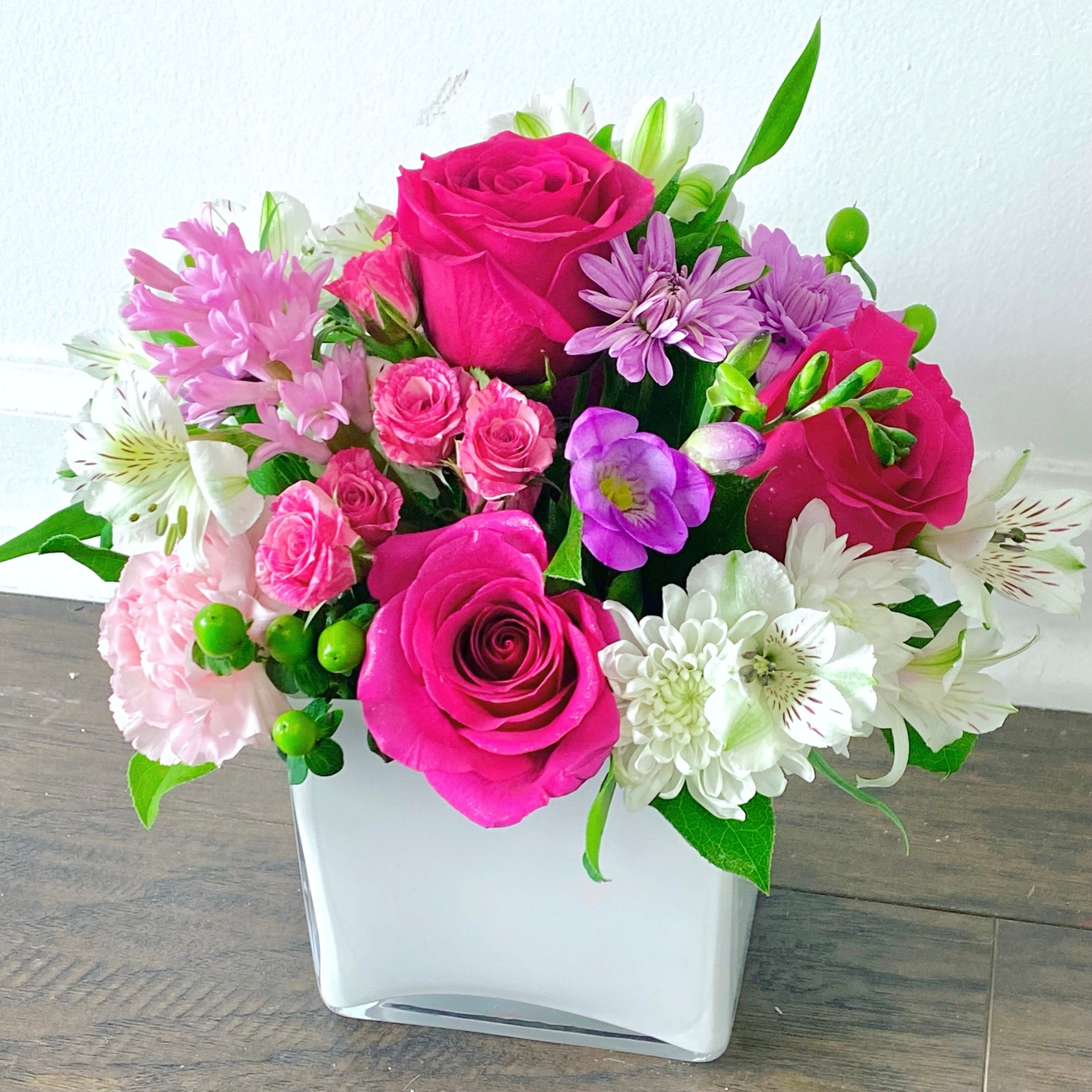 Bouquet of pink, purple, and white flowers in a white vase on a wooden surface for sunny isles flower delivery
