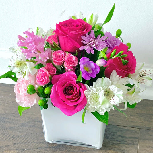 Bouquet of pink, purple, and white flowers in a white vase on a wooden surface for sunny isles flower delivery