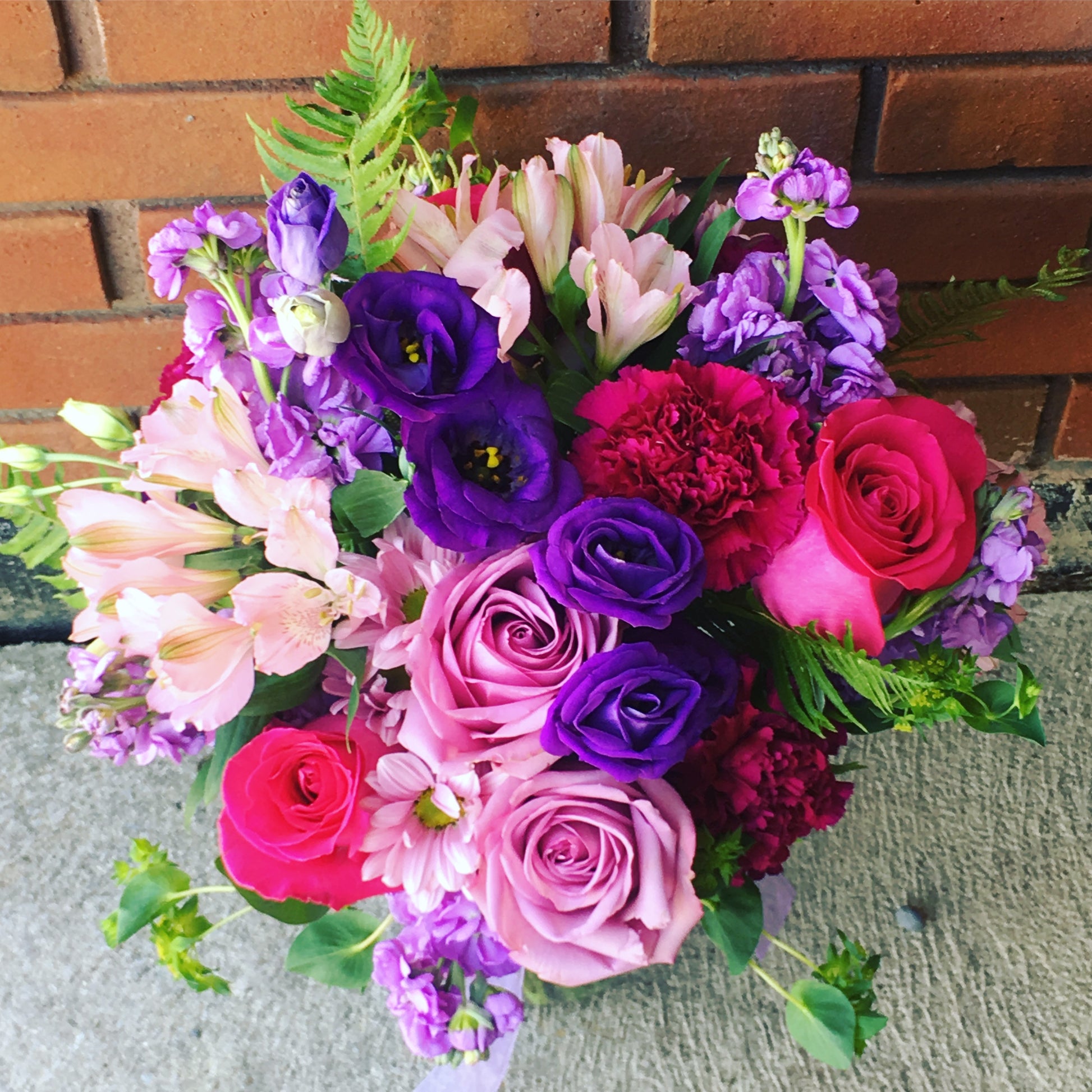 Send flowers of this bouquet of colorful flowers including roses and hydrangeas against a brick wall in Miami