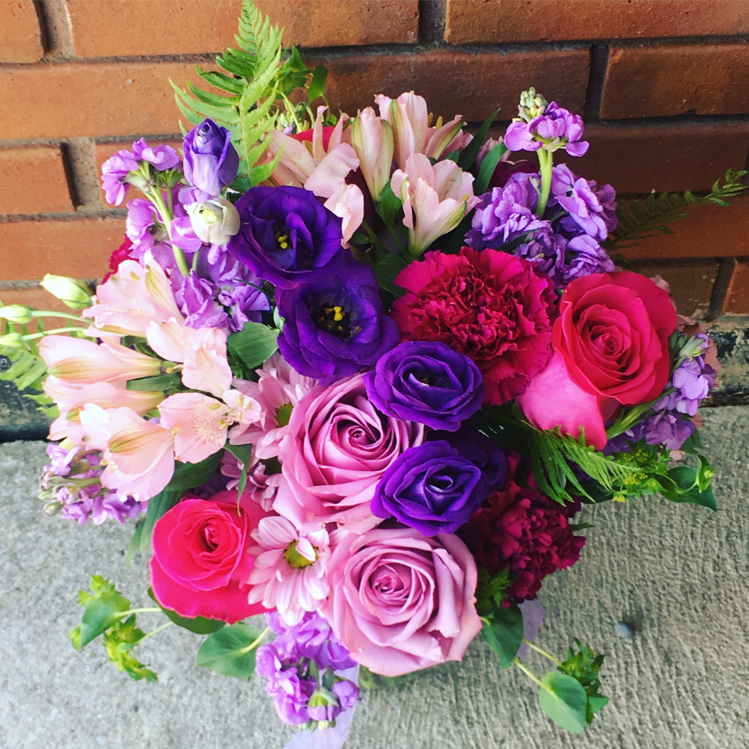 Send flowers of this bouquet of colorful flowers including roses and hydrangeas against a brick wall in Miami