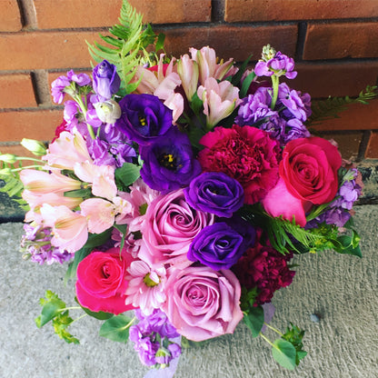 Send flowers of this bouquet of colorful flowers including roses and hydrangeas against a brick wall in Miami